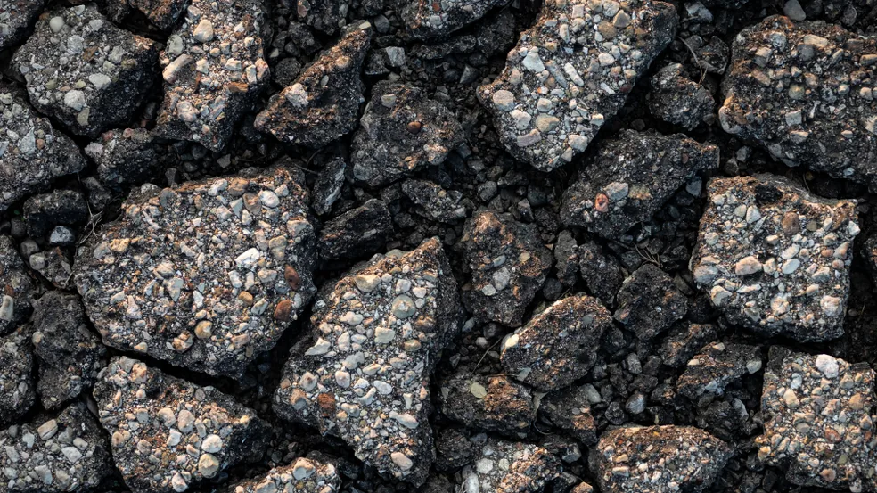 Badly deteriorated asphalt broken into loose interconnected fragments, the coarse stone aggregate exposed along every crack